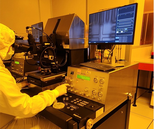 Technicien en salle blanche pilotant une station de test sous microscope, écran affichant l'inspection d'une puce